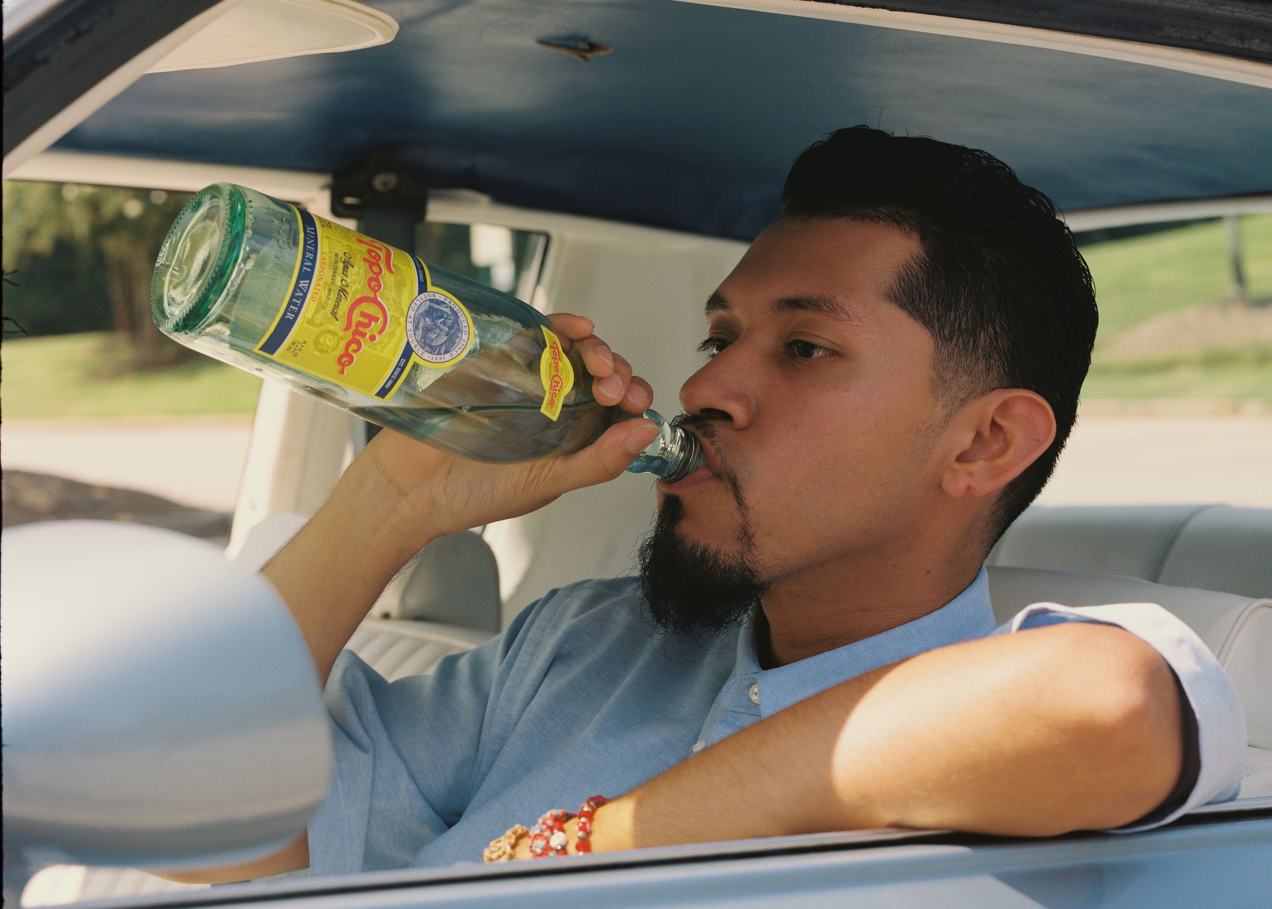 Corona relaxes in his car, drinking a bottle of Topo Chico mineral water from Mexico