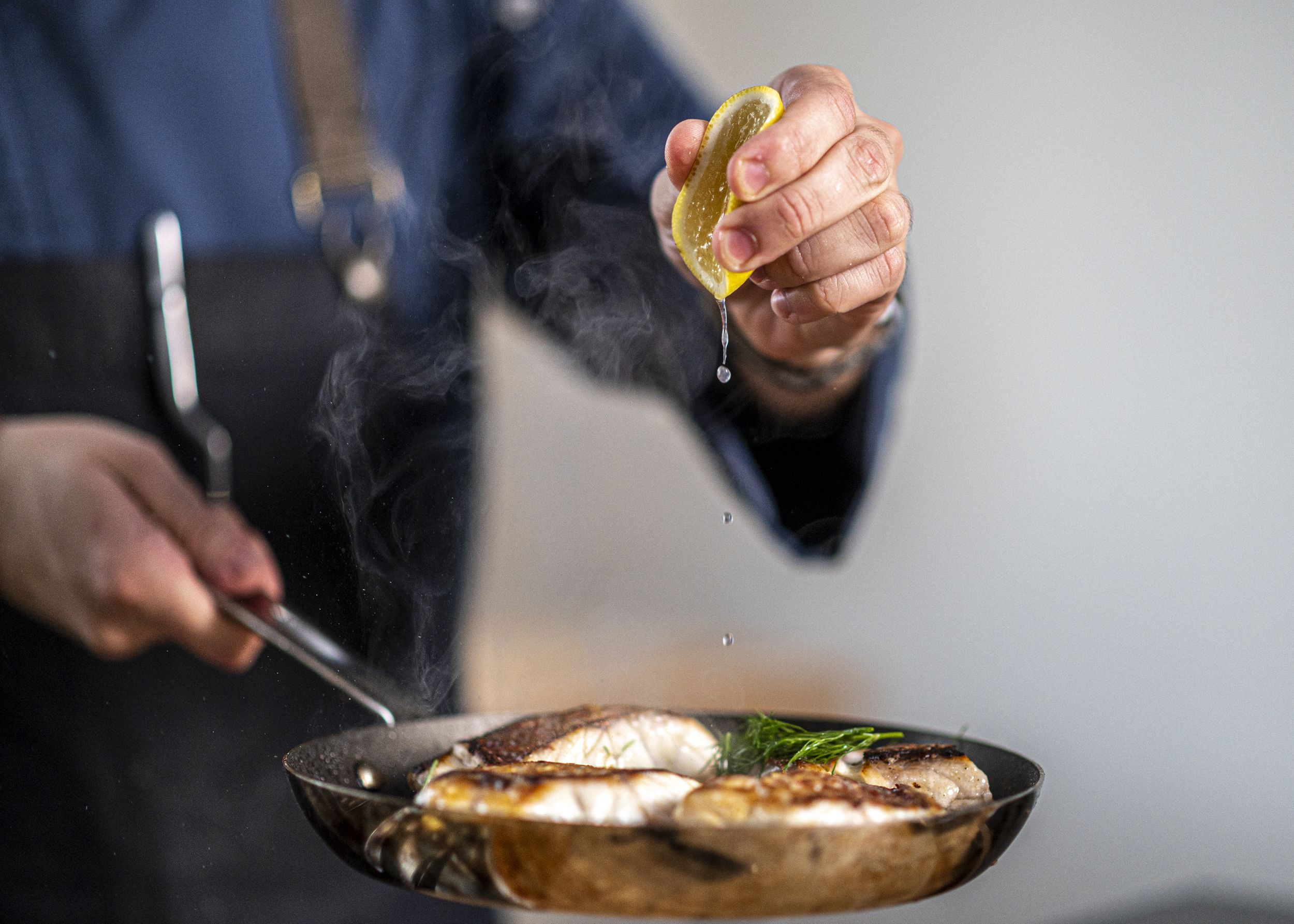 Chef Pereney squeezes lemon onto fish fillets in a pan.