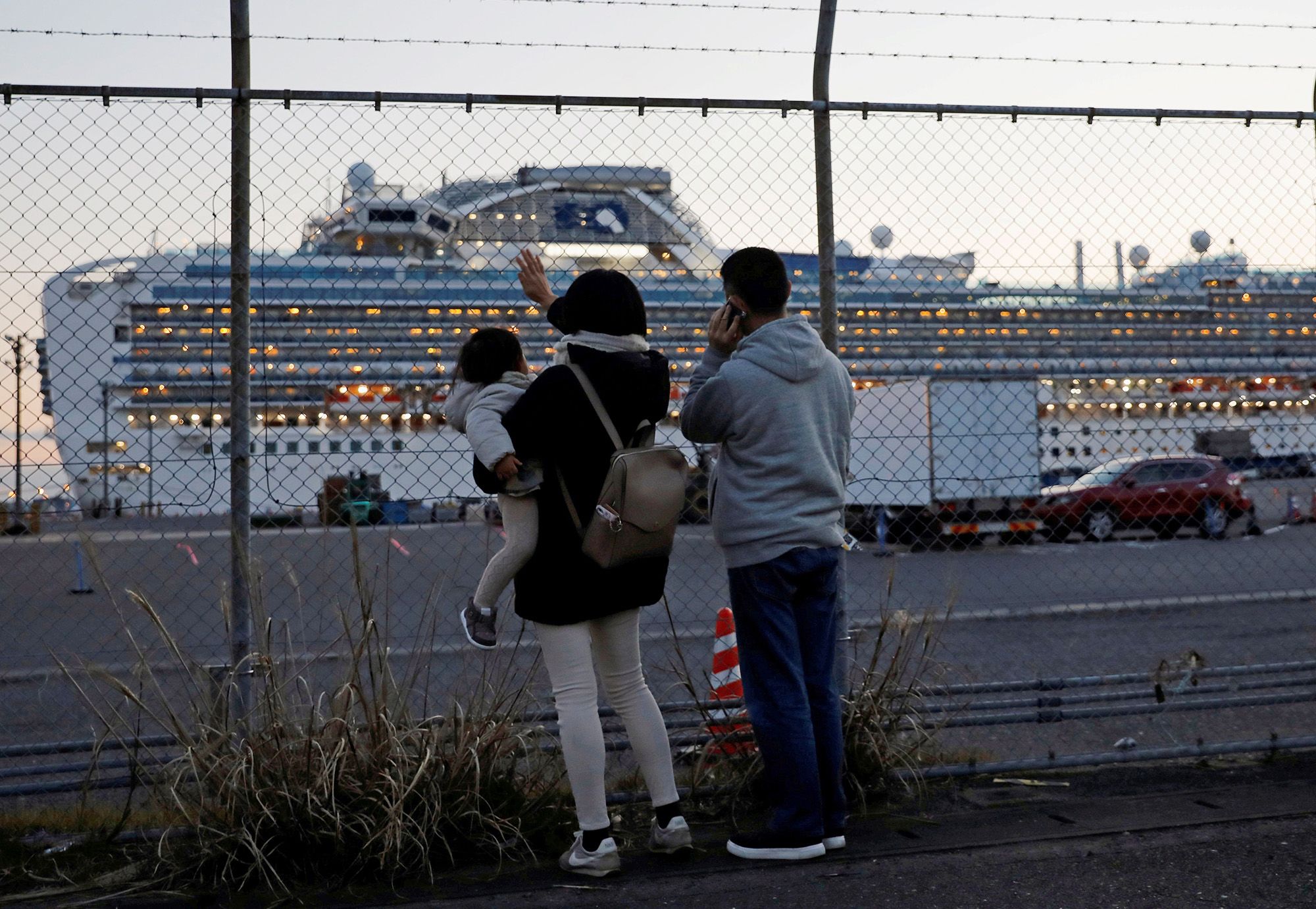 Family members of passengers onboard the cruise ship Diamond Princess wave and talk to them on the phone at a cruise terminal in Yokohama, Japan.