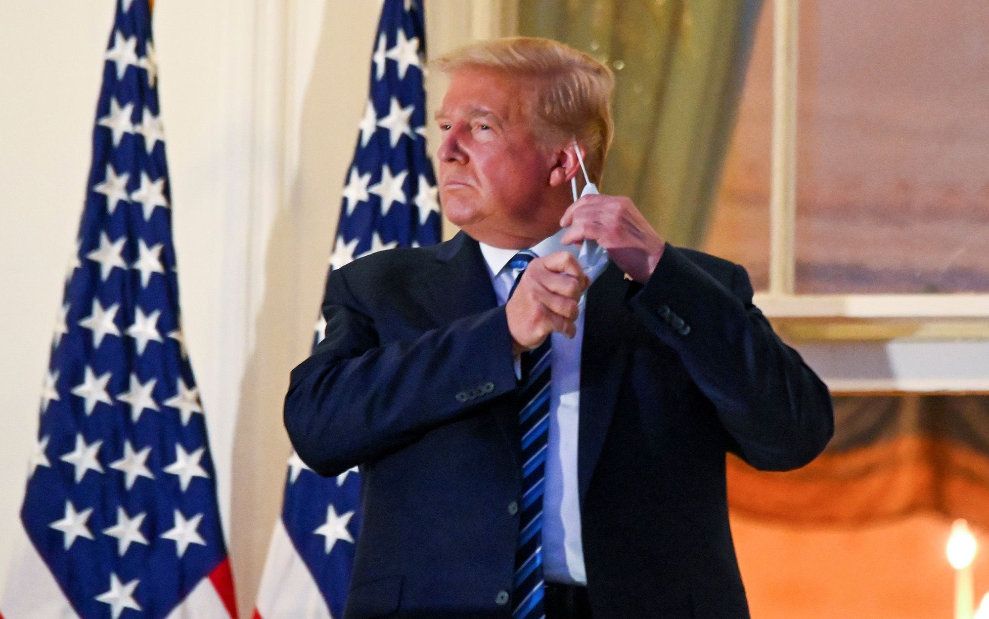 President Donald Trump pulls off his mask as he poses at the White House on Oct. 5 after returning from Walter Reed Medical Center where he received treatment for the coronavirus.