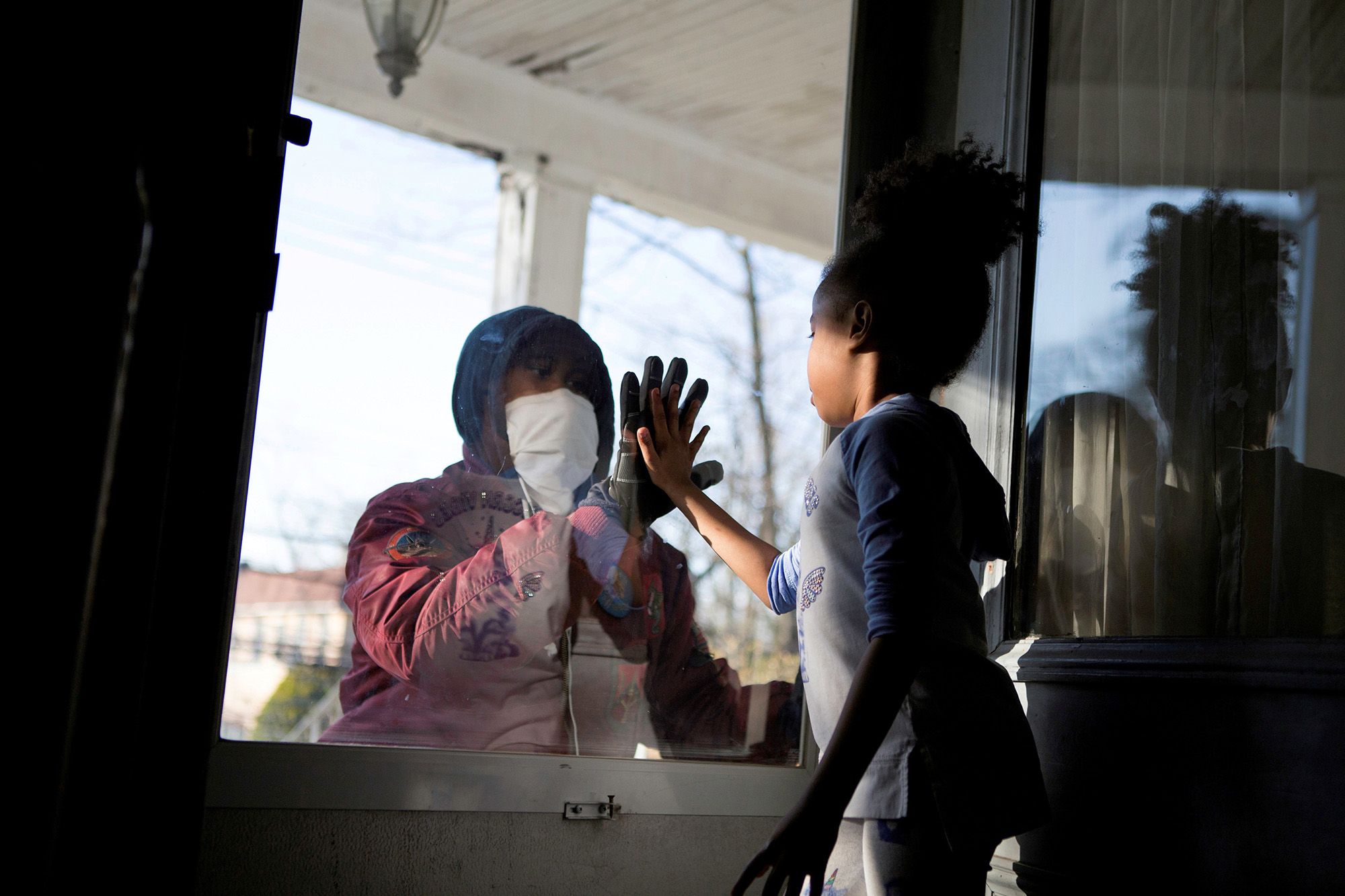 Hashim, an essential worker in the healthcare industry, greets his daughter through the closed door as he maintains social distance from his family in New Rochelle, N.Y.